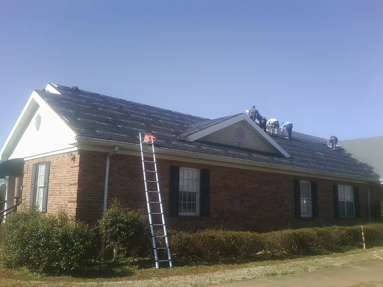 Crew tearing shingles off a brick ranch roof with a ladder set — Emergency Roof Repair work by our crew in Jonesville