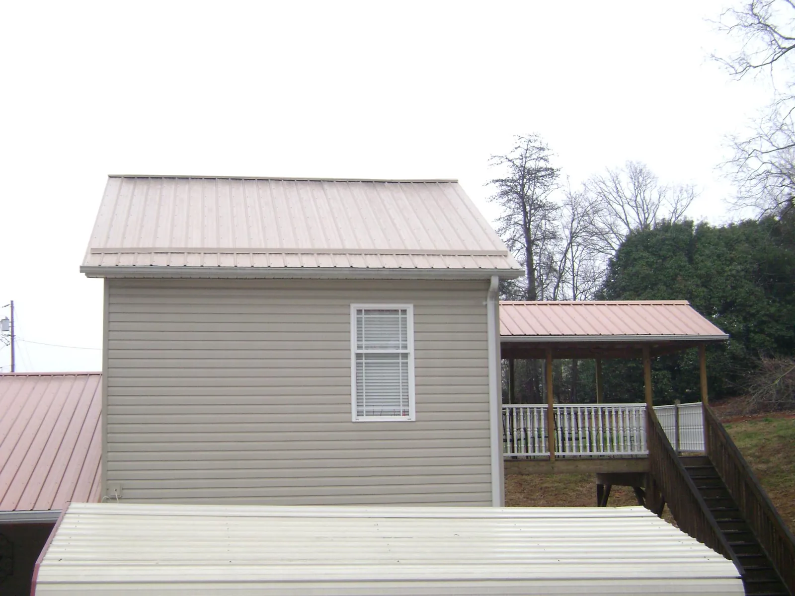 Tan metal roofs on a two story addition and attached porch, from a Roof Replacement job in Jonesville